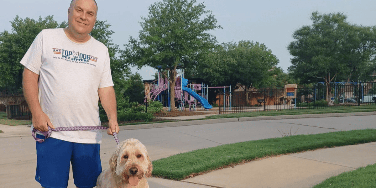 Friendly dog walker with Top Dog Pet Sitters logo in a park setting. Dog walker with a golden retriever in a park during daytime.